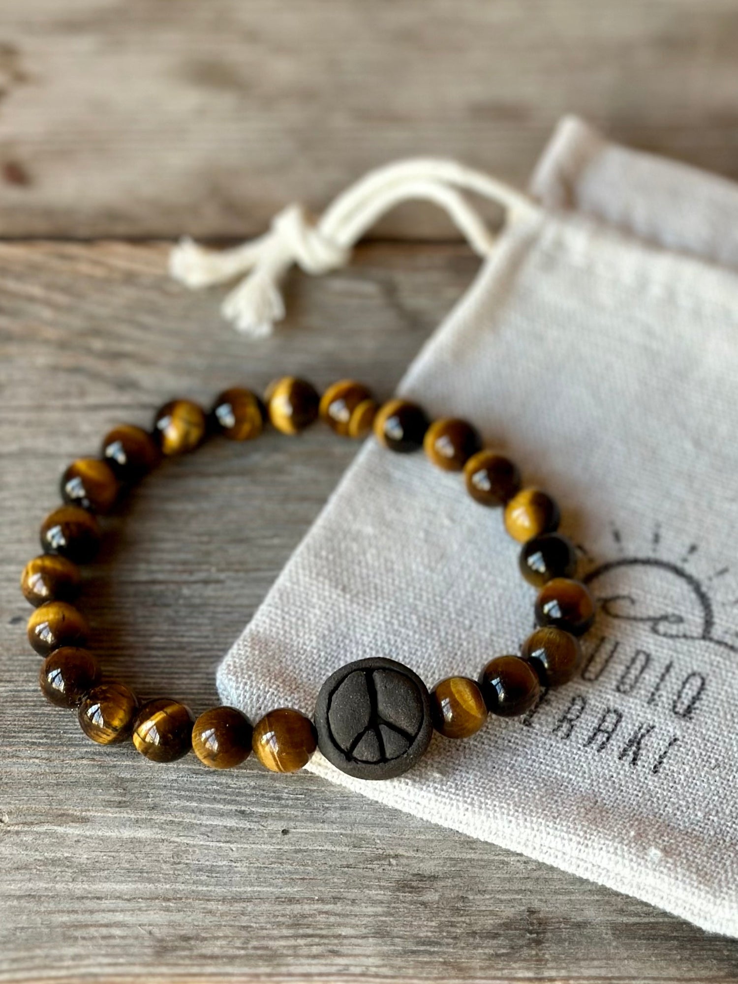 Studio Meraki bacelet with tiger's eye chrystal pearls and a raw ceramic pearl with a peace sign.