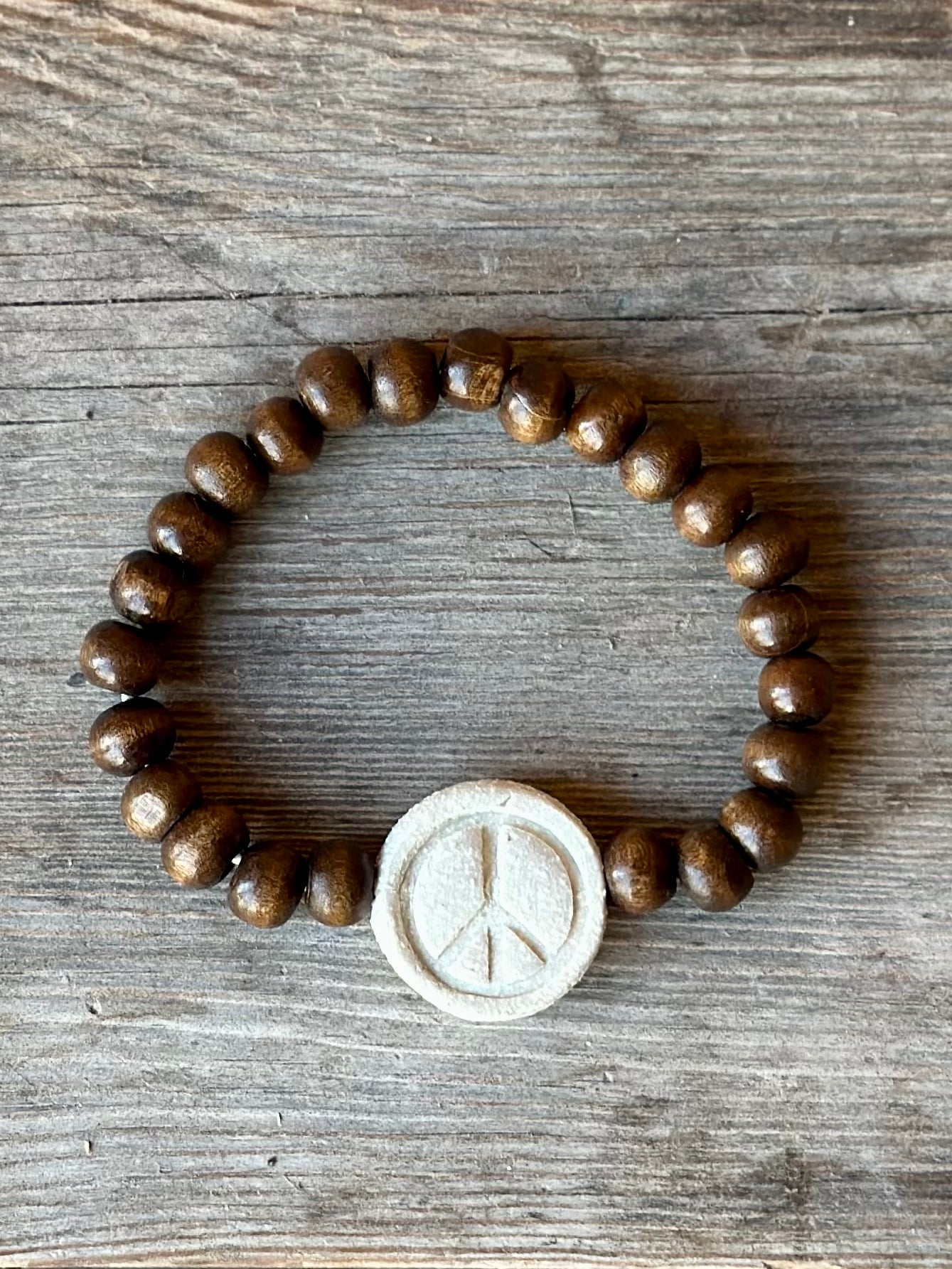 Studio Meraki bacelet with wood pearls and a raw ceramic pearl with a peace sign.