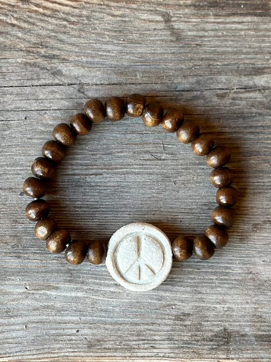 Studio Meraki bacelet with wood pearls and a raw ceramic pearl with a peace sign.
