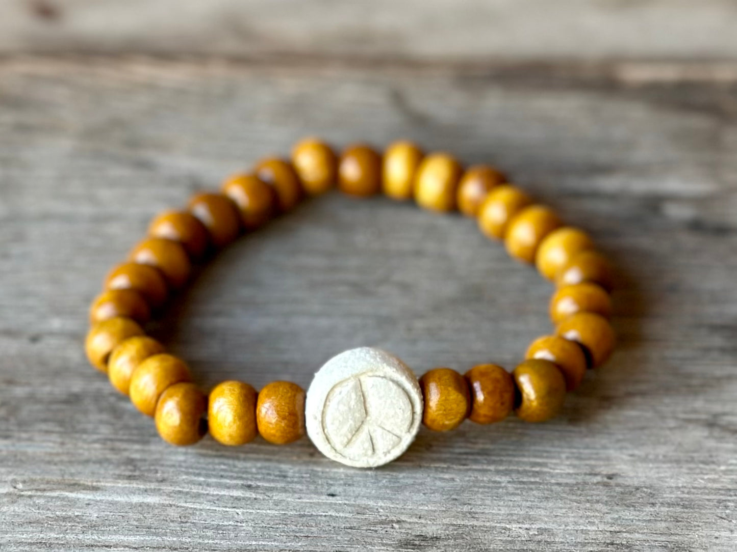 Studio Meraki bacelet with wood pearls and a raw ceramic pearl with a peace sign.