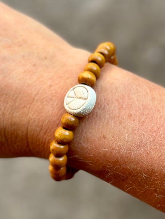 Studio Meraki bacelet with wood pearls and a raw ceramic pearl with a peace sign.