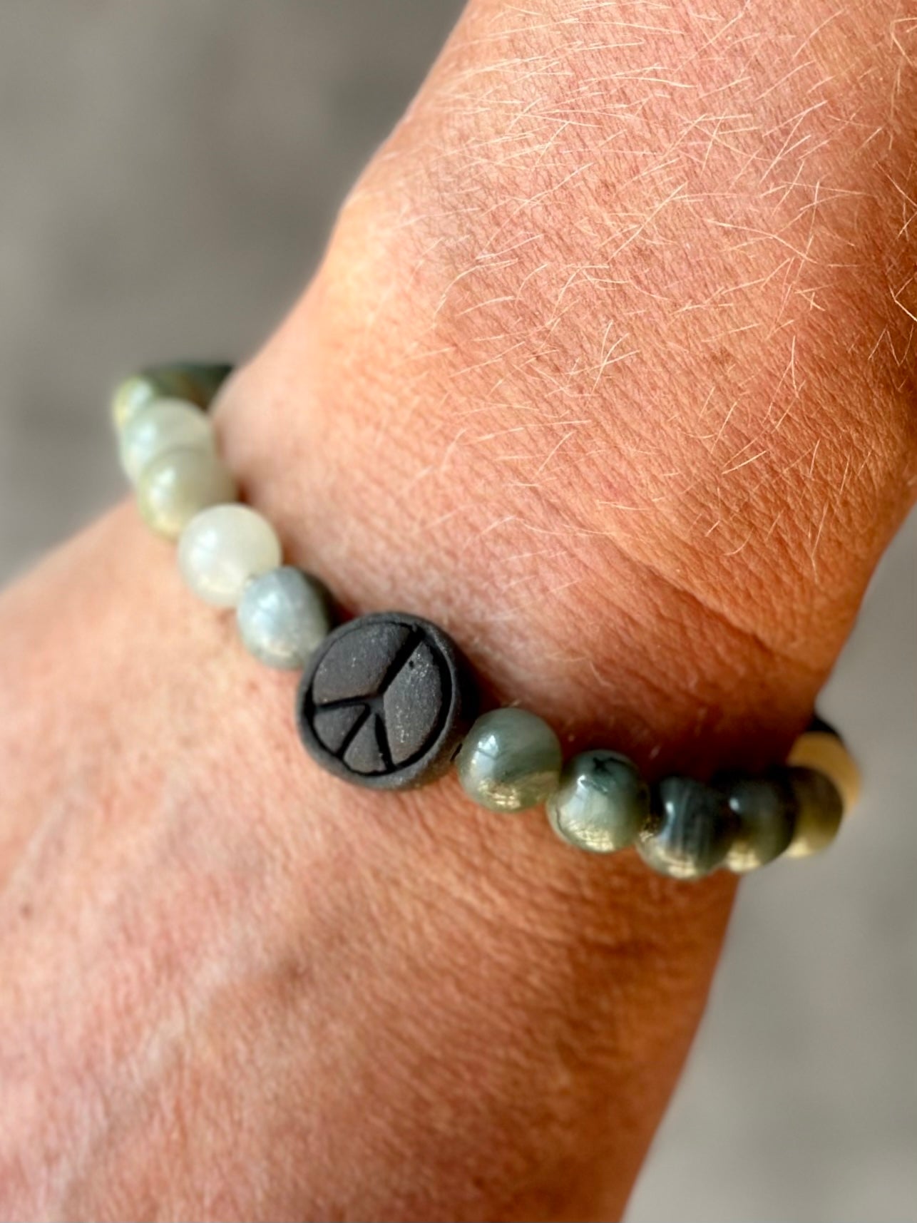 Studio Meraki bacelet with agate chrystal pearls and a raw ceramic pearl with a peace sign.