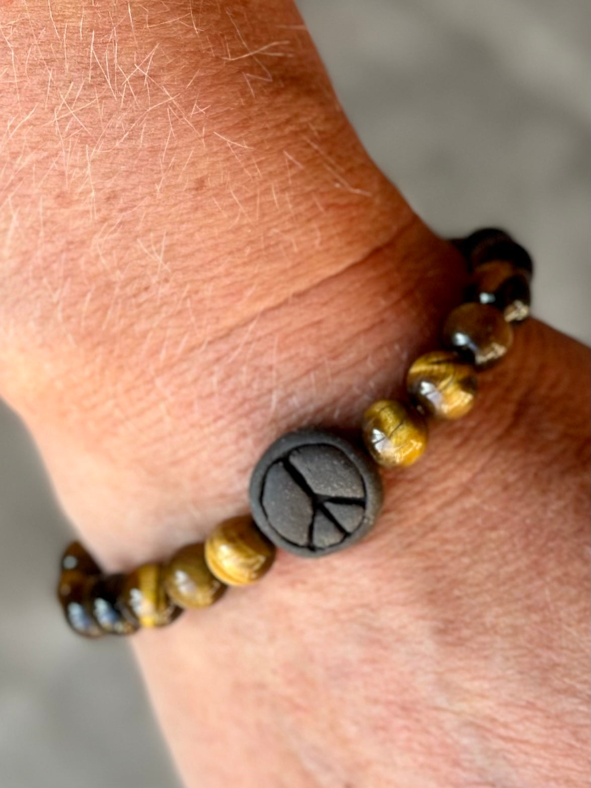 Studio Meraki bacelet with tiger's eye chrystal pearls and a raw ceramic pearl with a peace sign.
