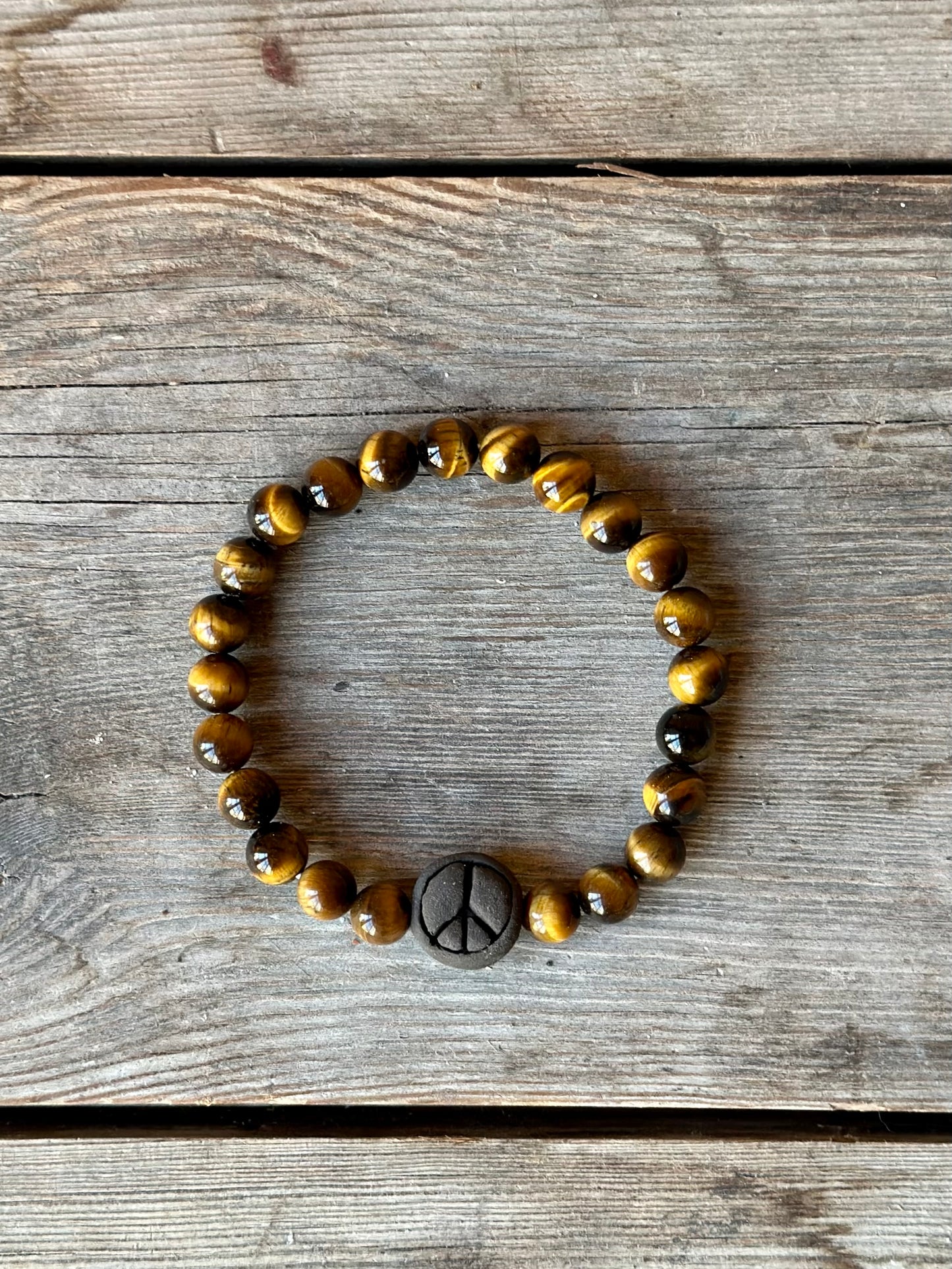 Studio Meraki bacelet with tiger's eye chrystal pearls and a raw ceramic pearl with a peace sign.