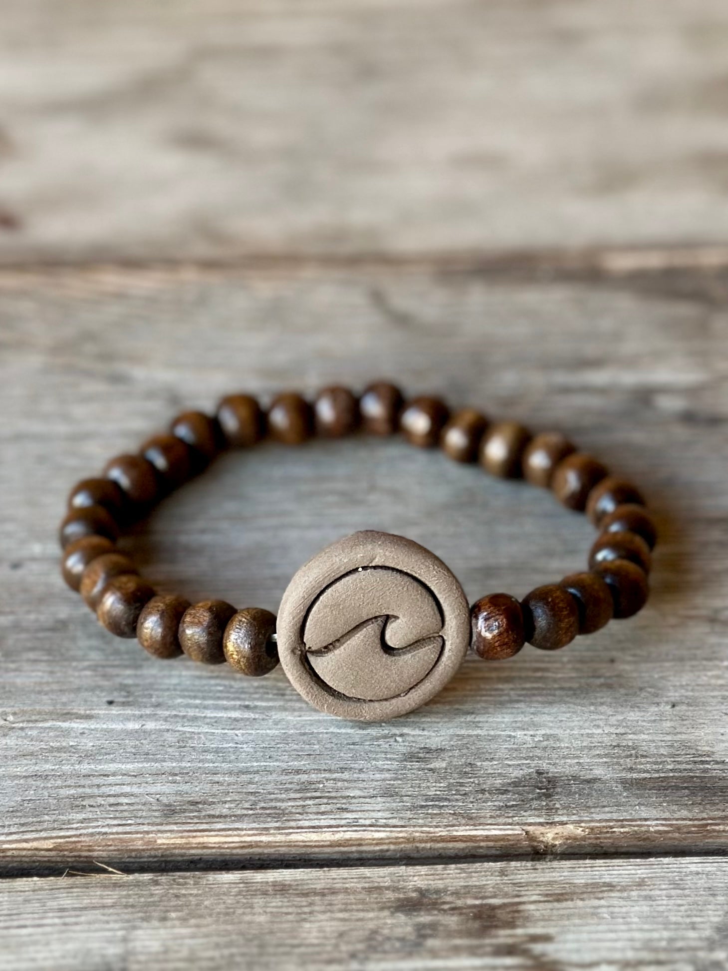 Studio Meraki bacelet with wood pearls and a raw ceramic pearl with a wave.