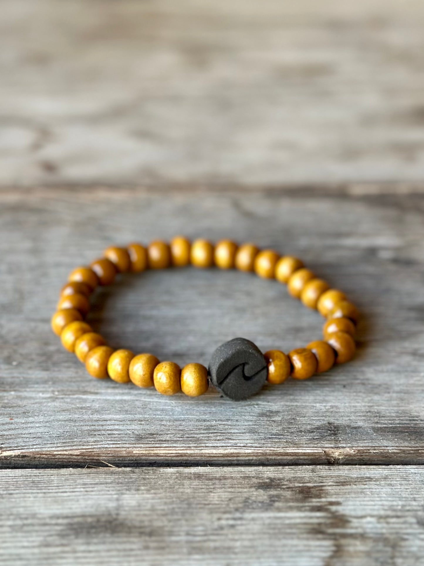 Studio Meraki bacelet with wooden pearls and a raw ceramic pearl with a wave.