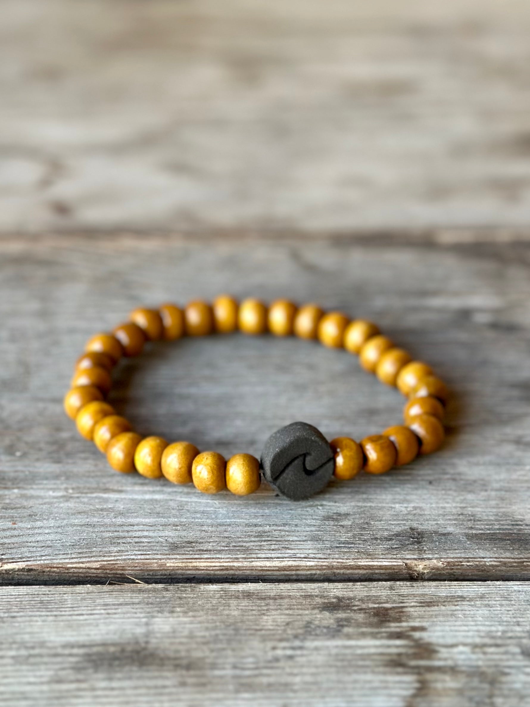 Studio Meraki bacelet with wooden pearls and a raw ceramic pearl with a wave.