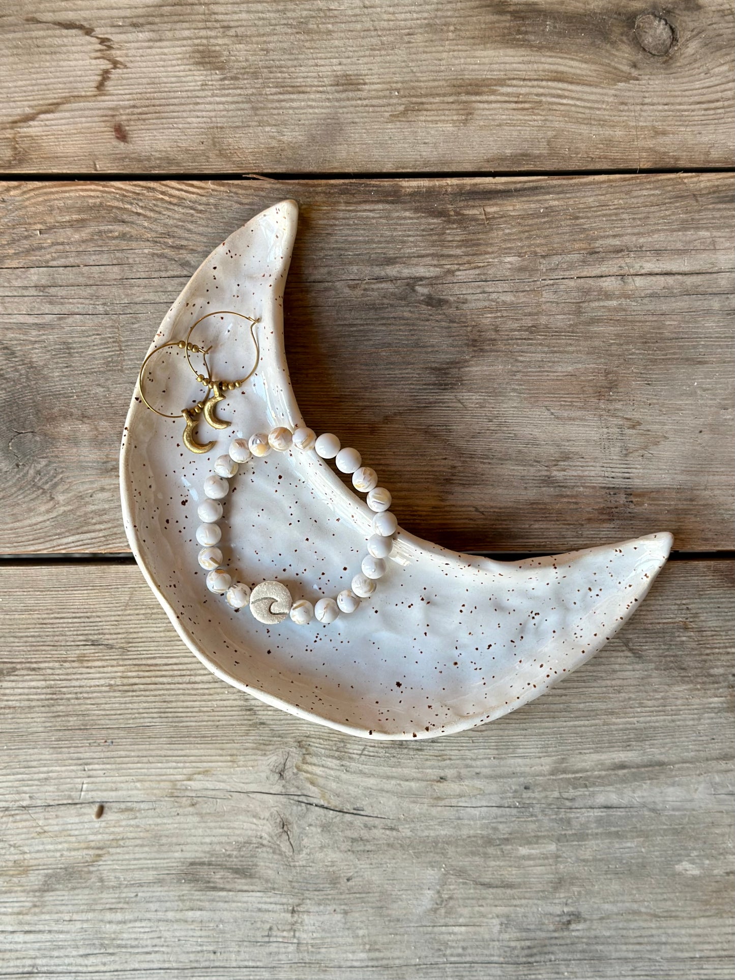Moon shaped ceramic tray with a pair of ear rings and a bracelet in howlite chrystal with a wave.