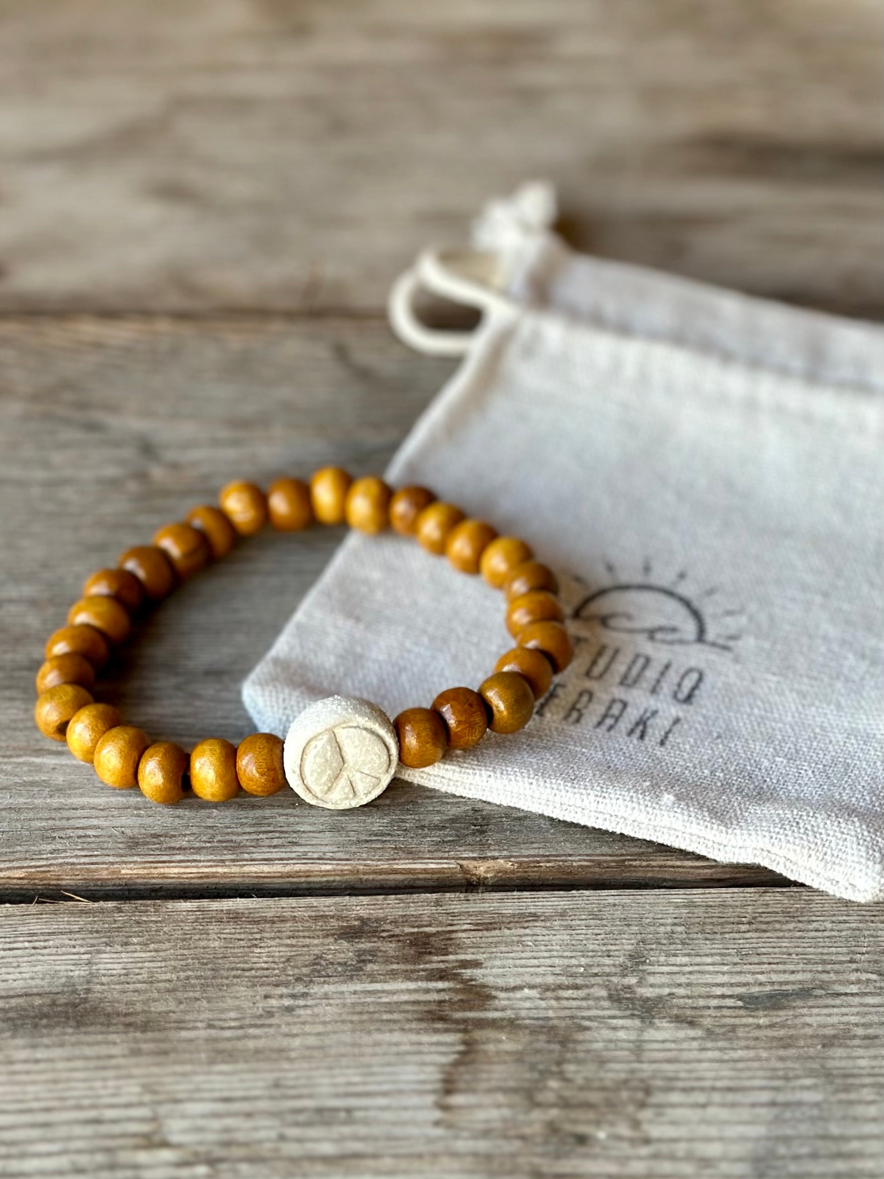 Studio Meraki bacelet with wood pearls and a raw ceramic pearl with a peace sign.