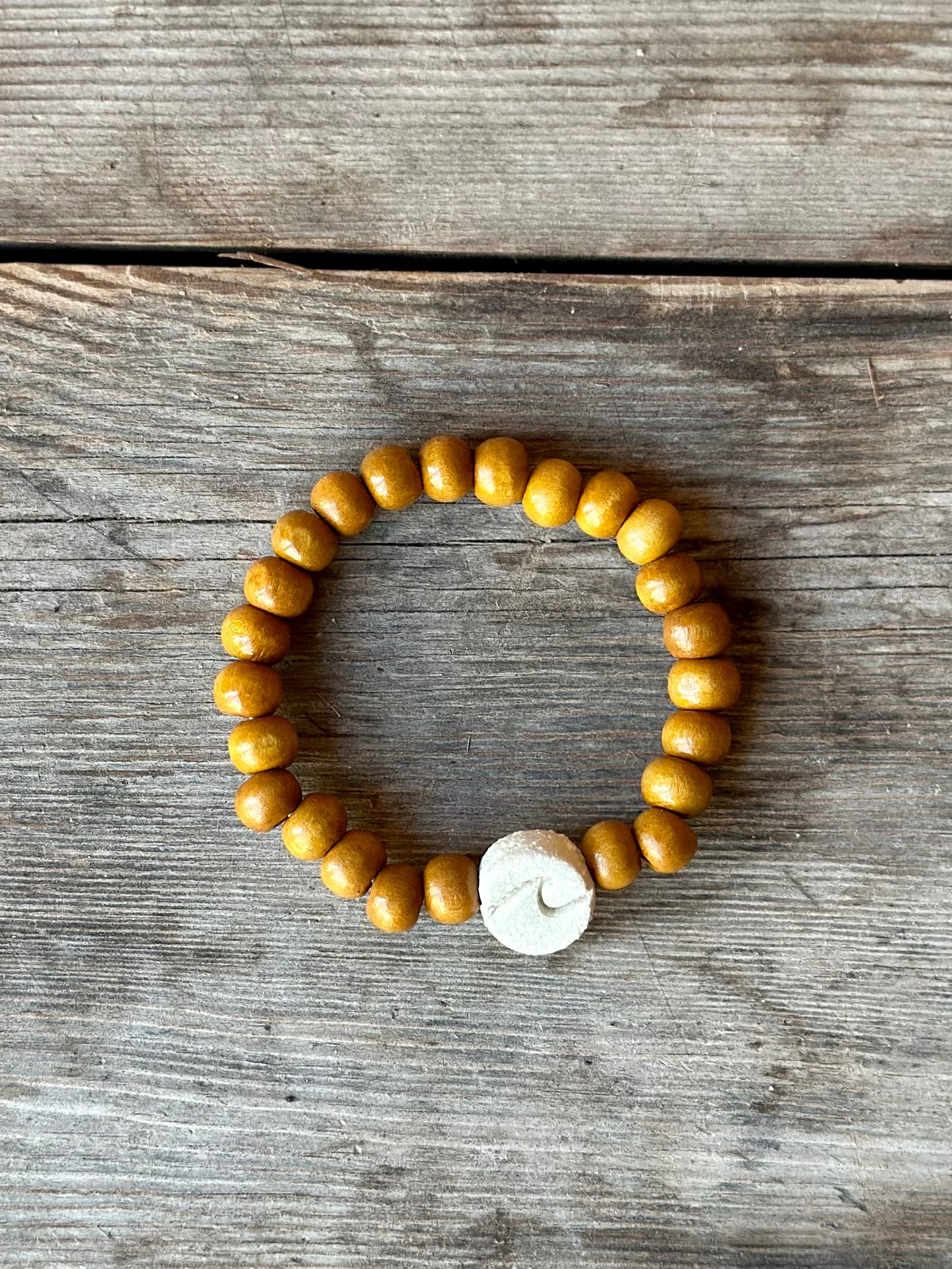 Studio Meraki bacelet with wood pearls and a raw ceramic pearl with a wave.