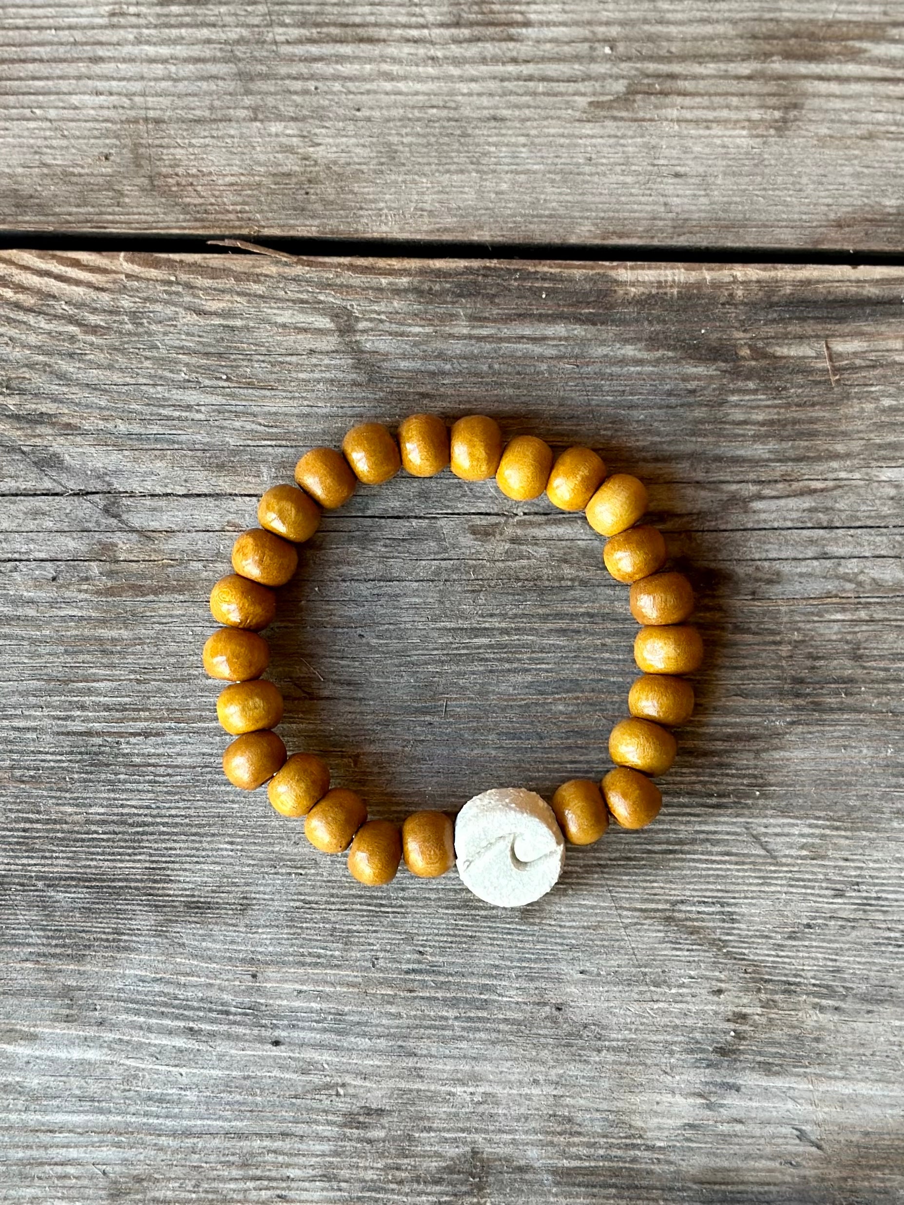 Studio Meraki bacelet with wood pearls and a raw ceramic pearl with a wave.