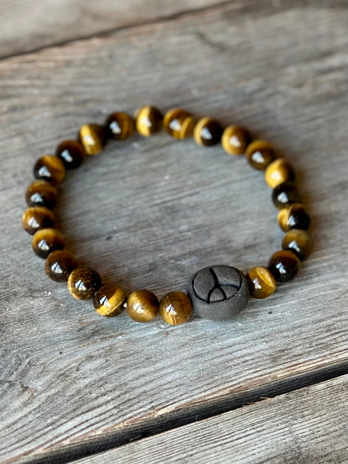 Studio Meraki bacelet with tiger's eye chrystal pearls and a raw ceramic pearl with a peace sign.