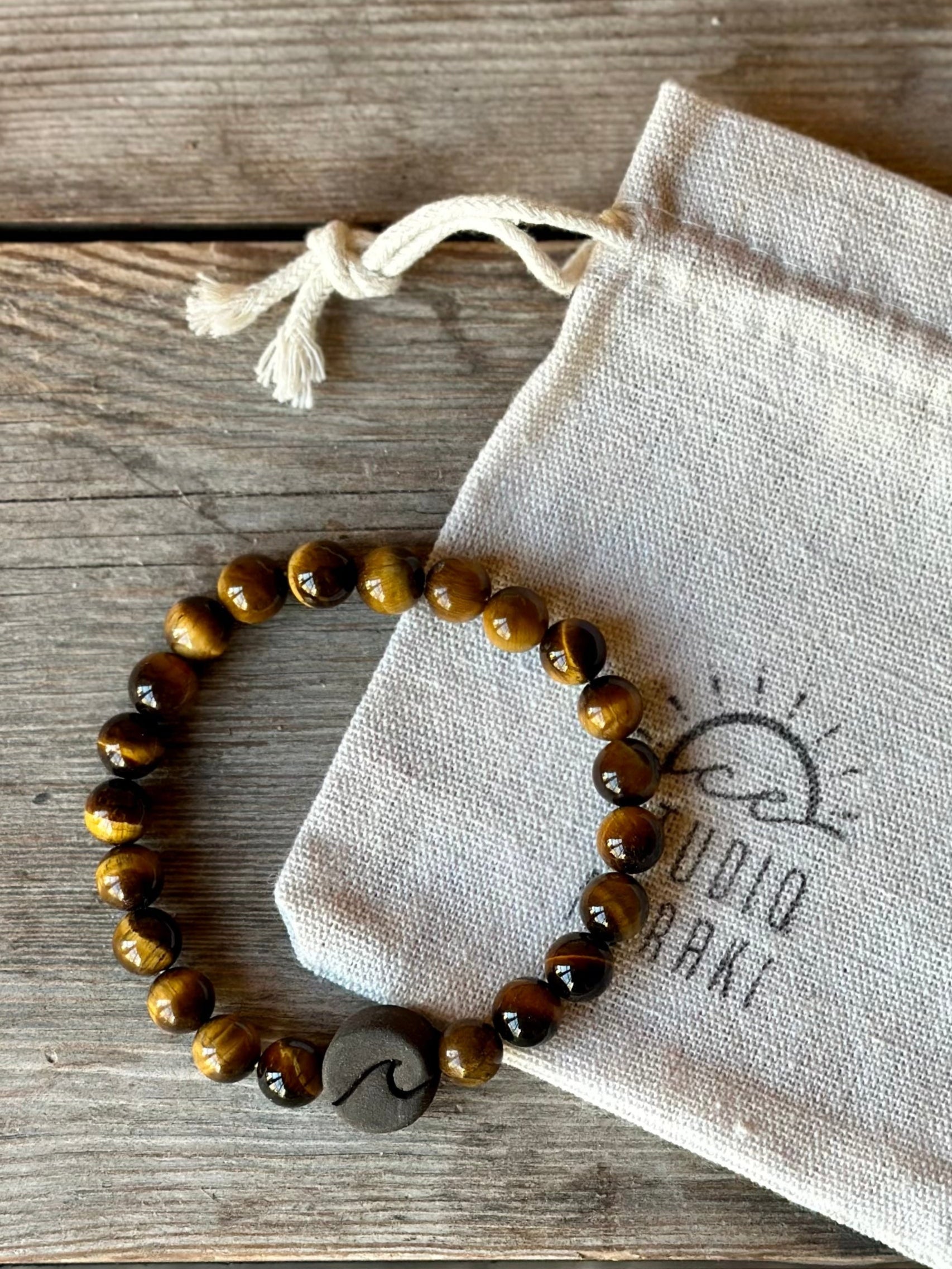 Studio Meraki bacelet with tiger's eya chrystal pearls and a raw ceramic pearl with a wave.