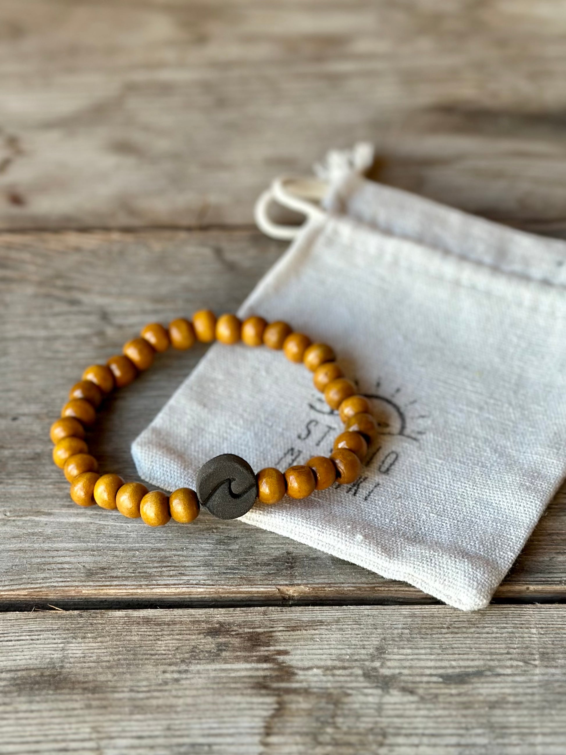 Studio Meraki bacelet with wood pearls and a raw ceramic pearl with a wave.