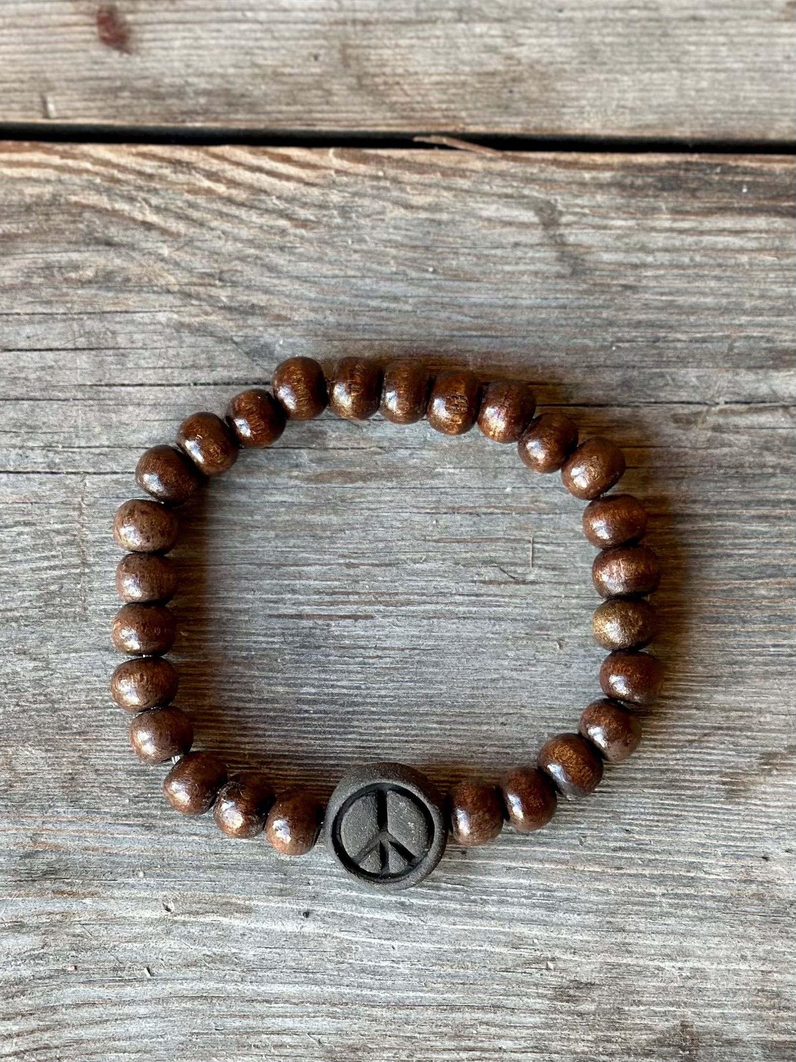 Studio Meraki bacelet with woodl pearls and a raw ceramic pearl with a peace sign.