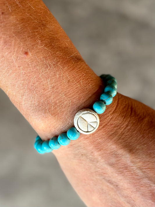 Studio Meraki bacelet with turqoise chrystal pearls and a raw ceramic pearl with a peace sign.