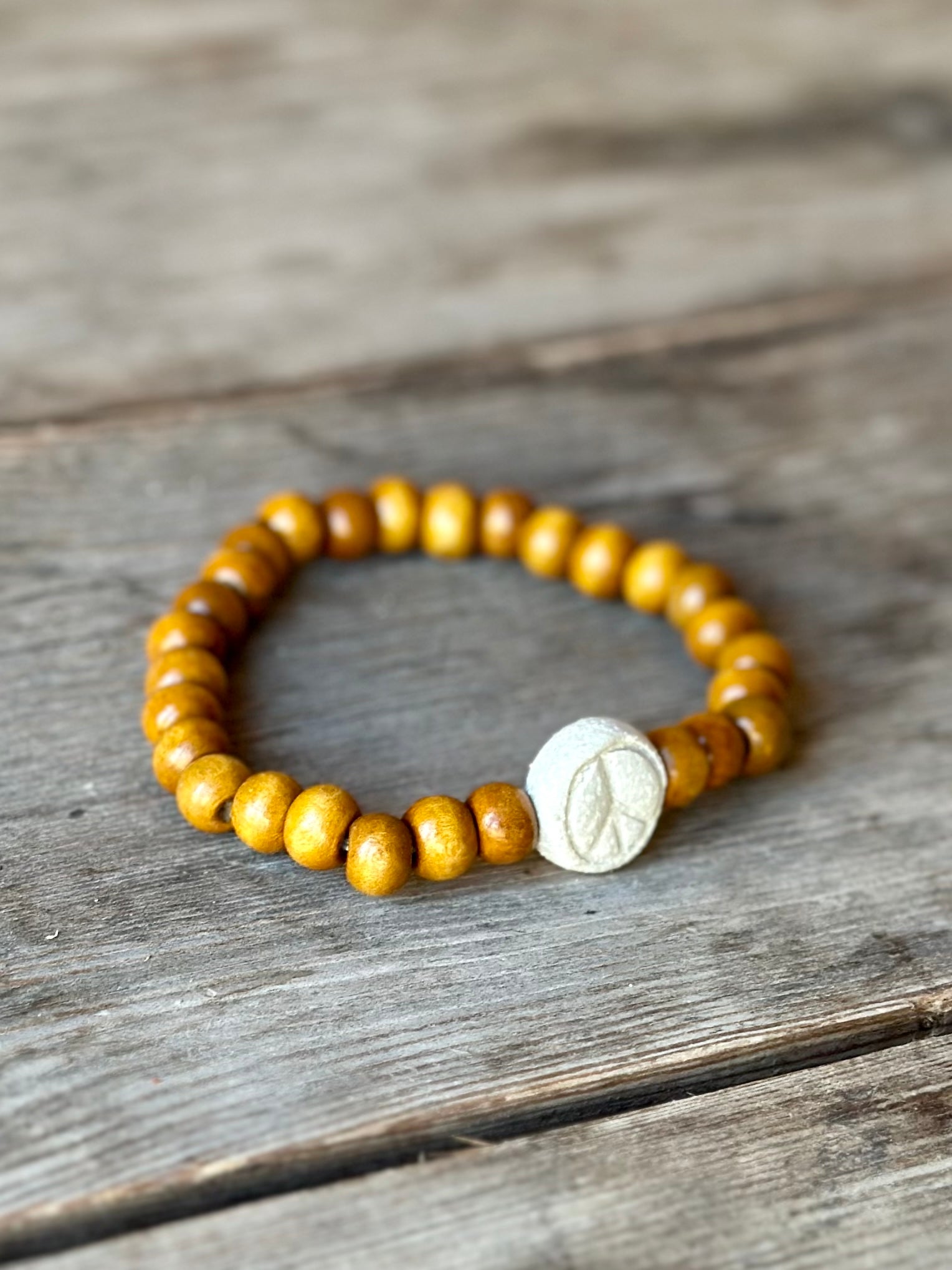 Studio Meraki bacelet with wood pearls and a raw ceramic pearl with a peace sign.