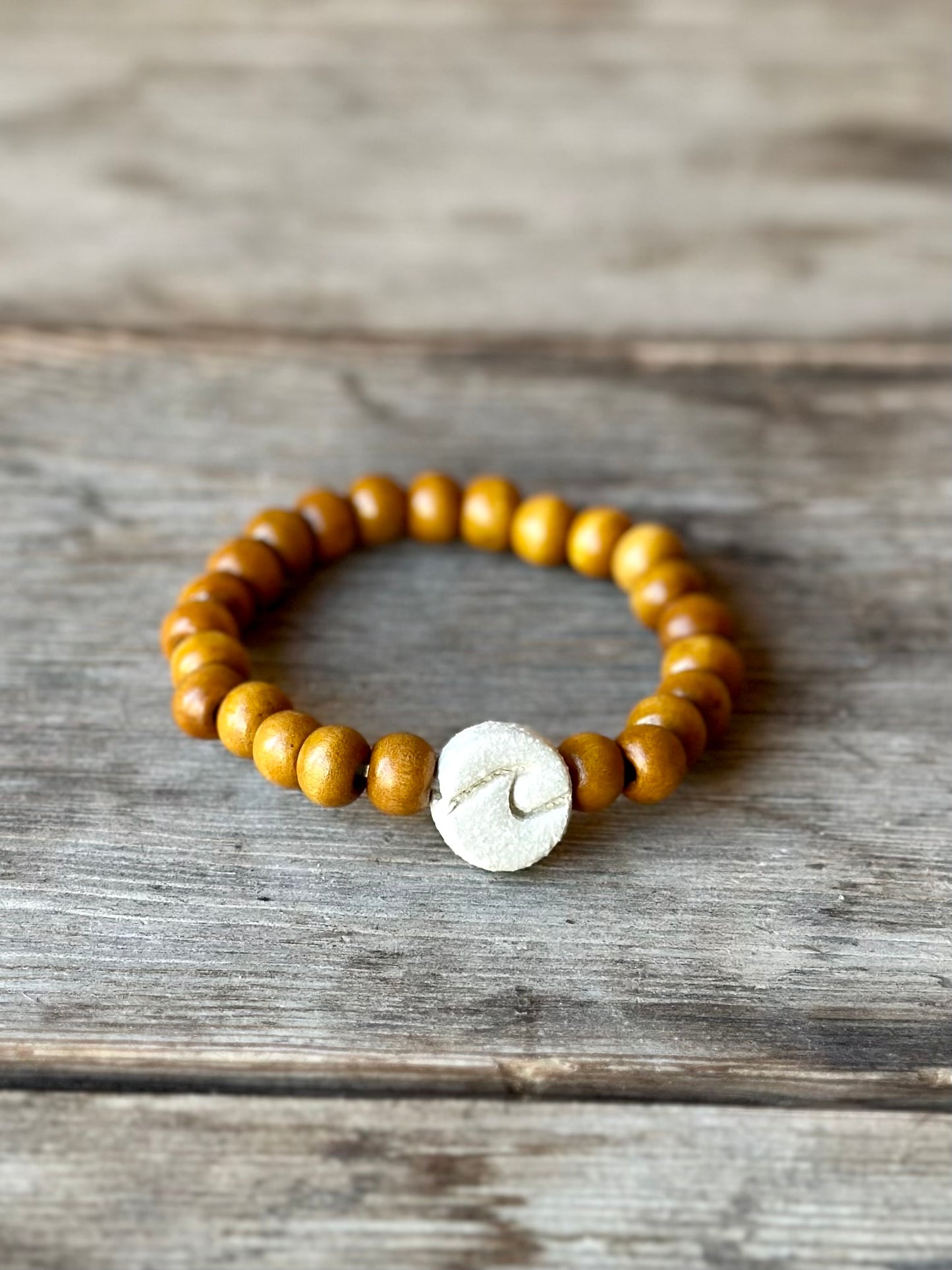 Studio Meraki bacelet with wood pearls and a raw ceramic pearl with a wave.
