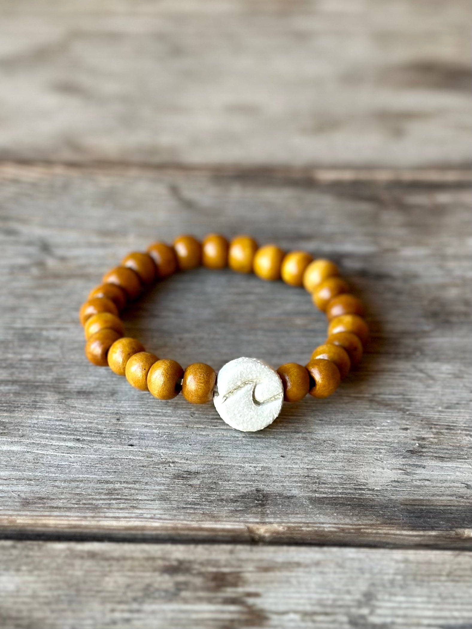 Studio Meraki bacelet with wood pearls and a raw ceramic pearl with a wave.