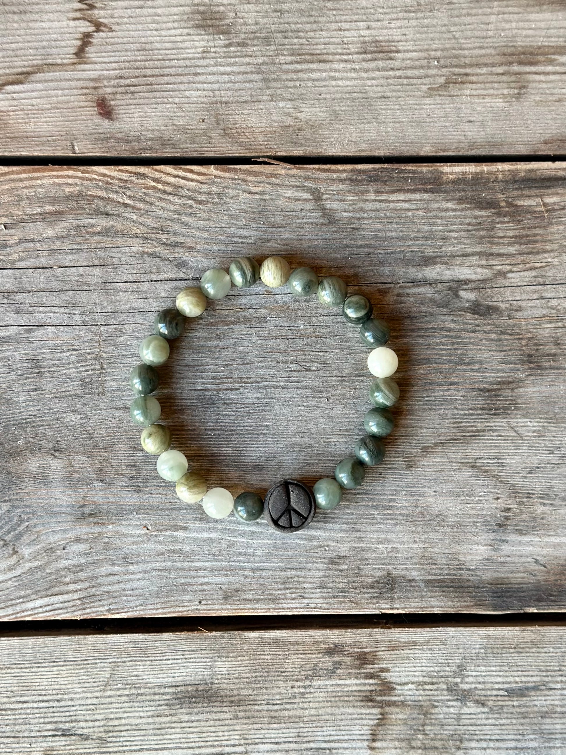 Studio Meraki bacelet with agate chrystal pearls and a raw ceramic pearl with a peace sign.