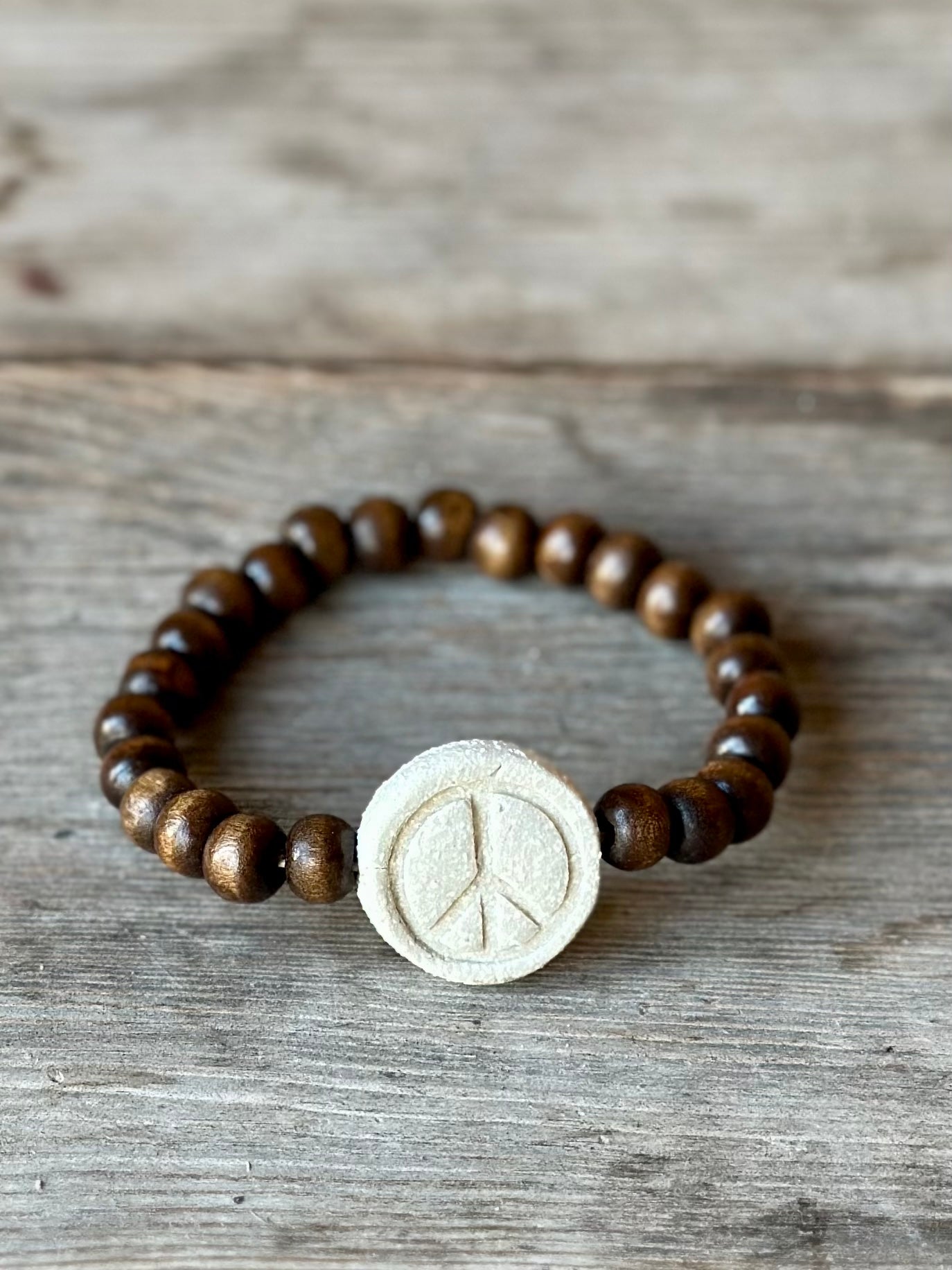 Studio Meraki bacelet with wood pearls and a raw ceramic pearl with a peace sign.