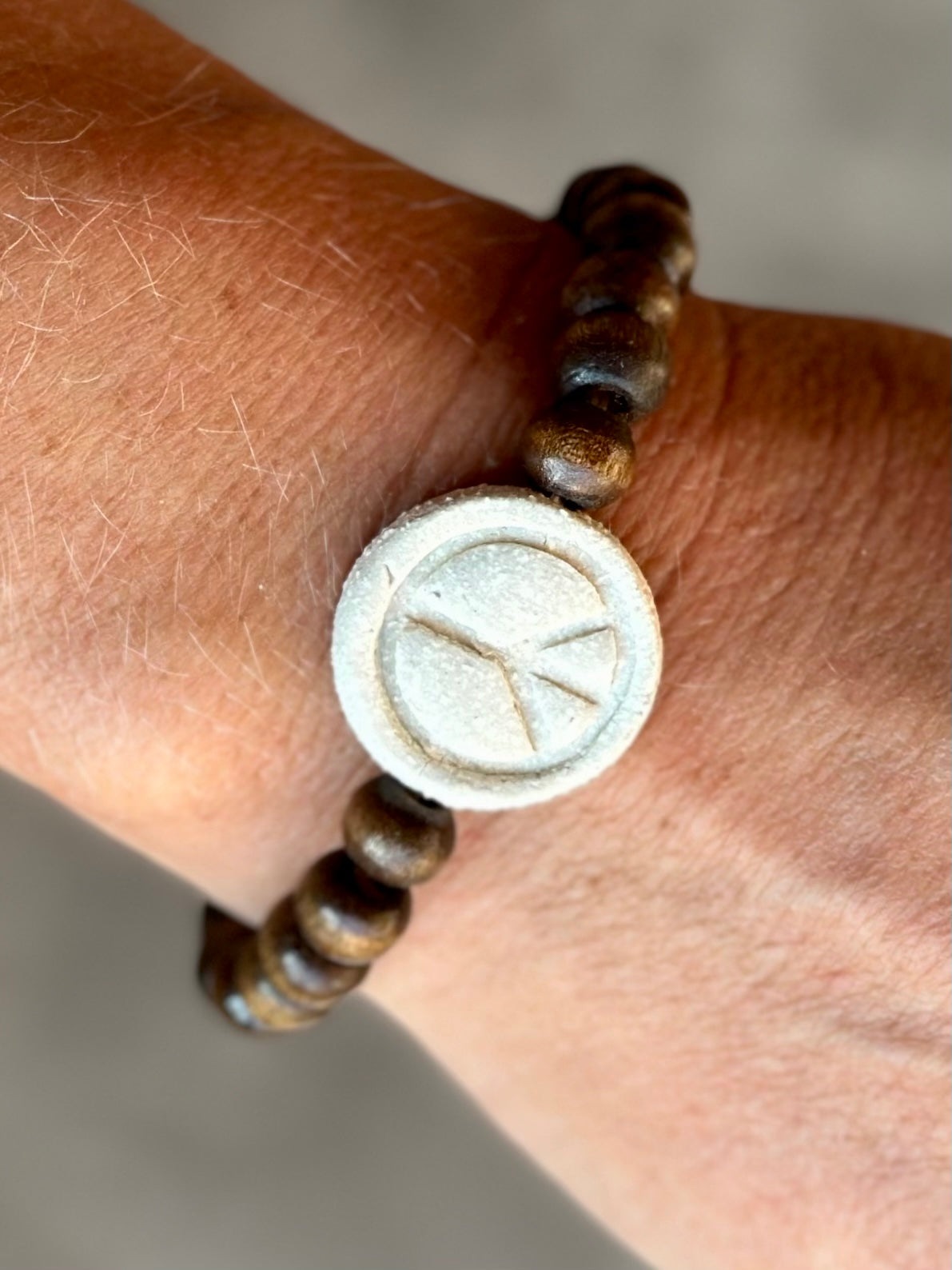 Studio Meraki bacelet with wood pearls and a raw ceramic pearl with a peace sign.