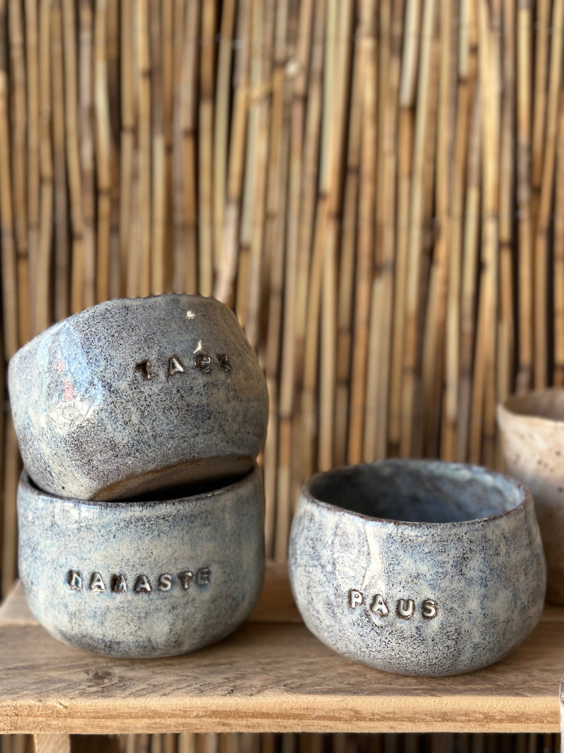 Ceramic mugs on a shelf. Decorated with words like Pause and Namaste.