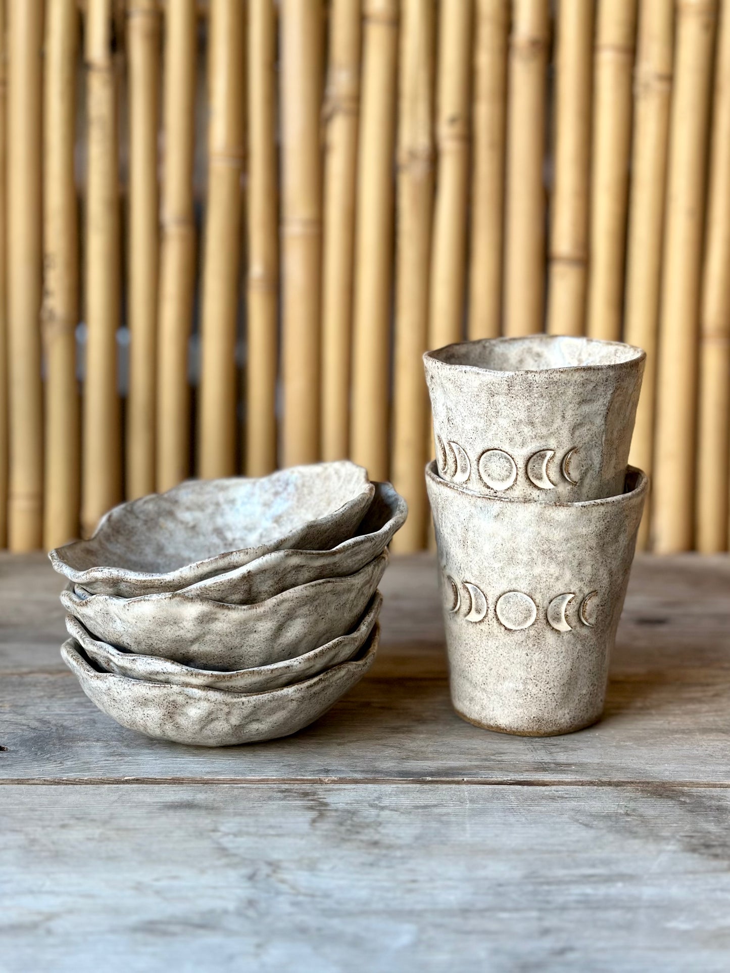 Ceramic bowls stack next to two ceramic mugs decorated with the moon phases, standing on a table.