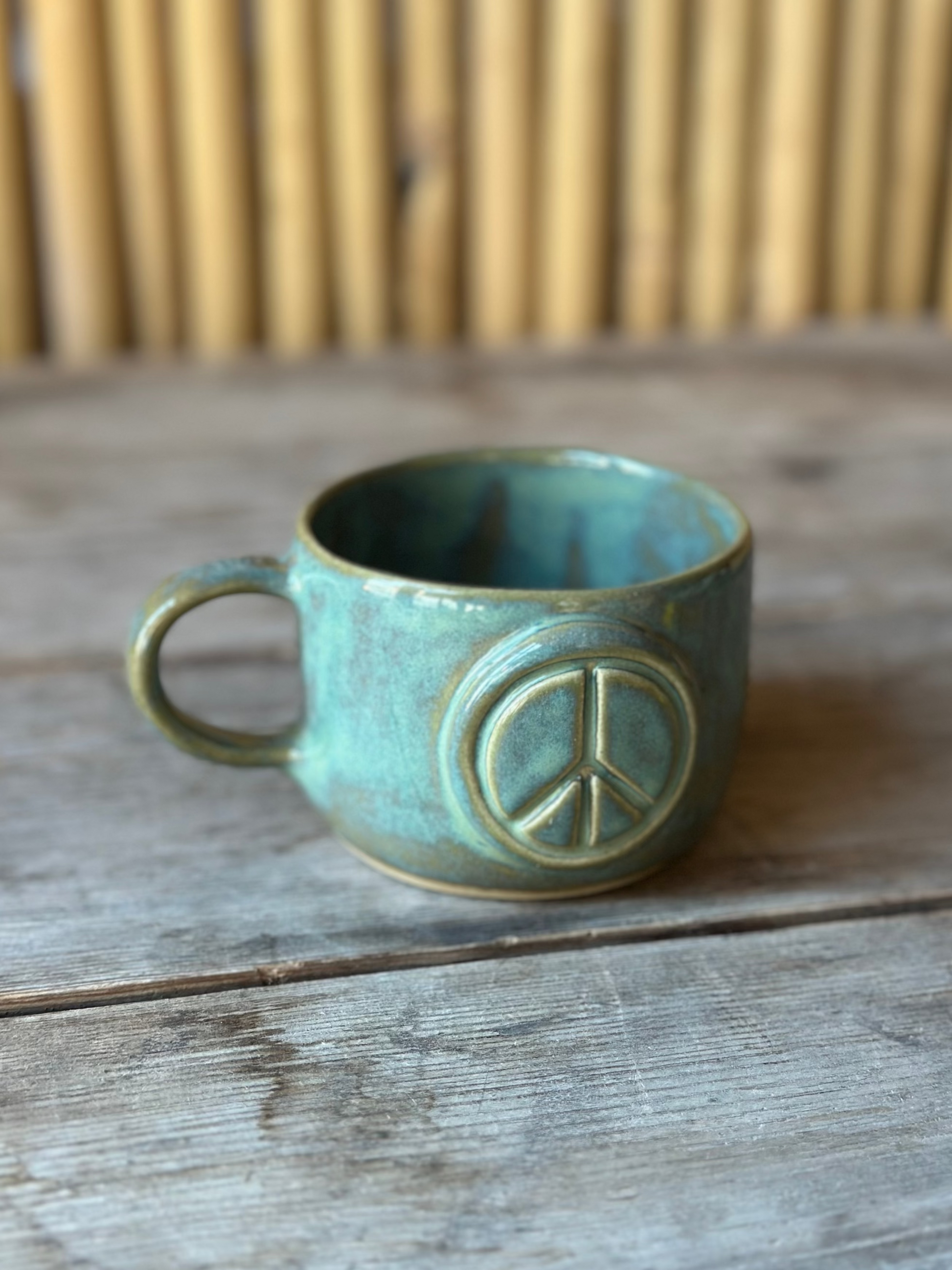 Green ceramic cup with handle, decorated with a peace sign.