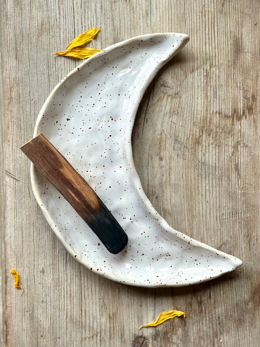 Moon shaped decorative ceramic tray with dark green glaze. On the tray lays a Palo Santo incense stick.