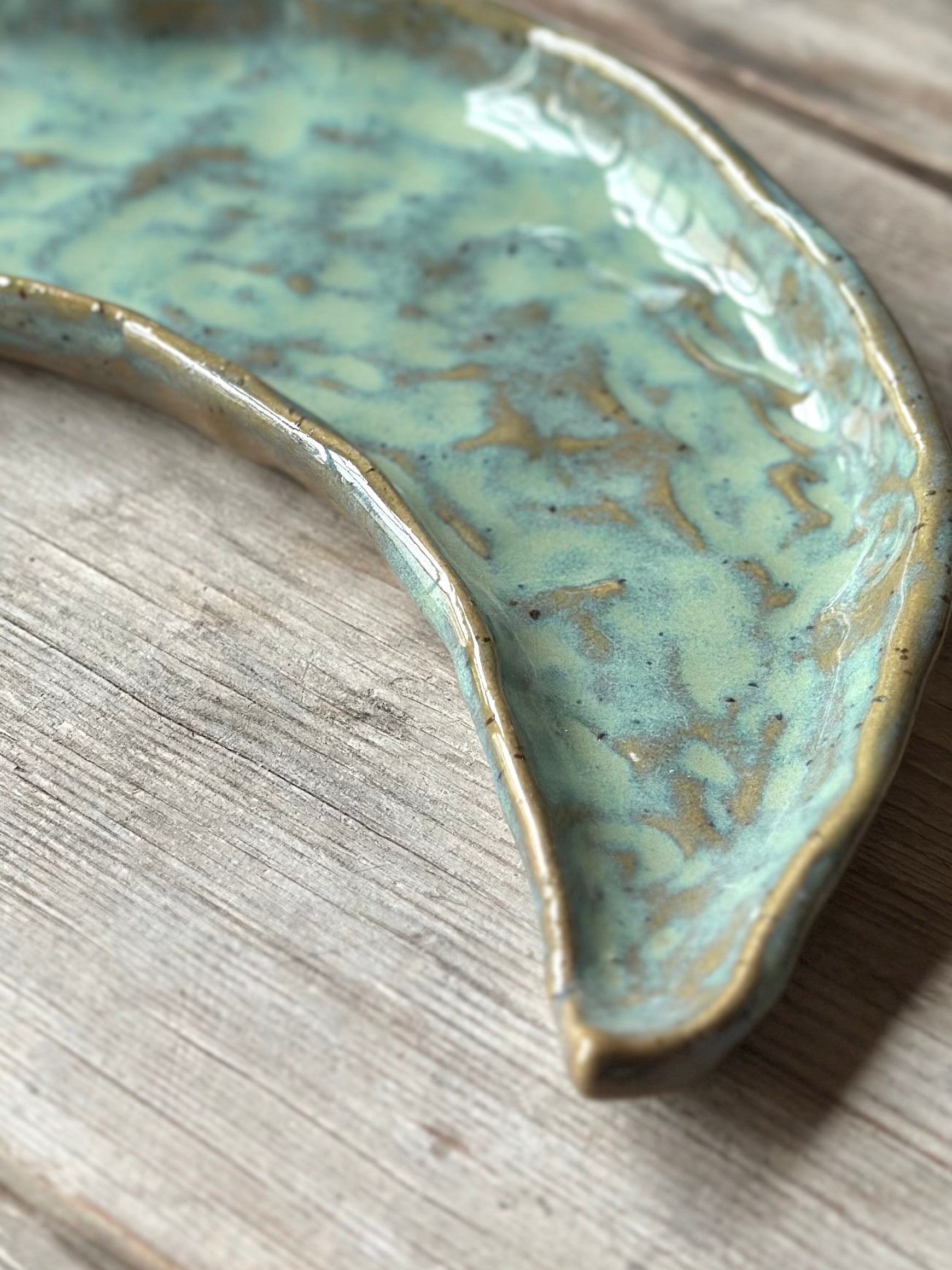 Close up on a moon shaped decorative tray with turqoise green glaze.