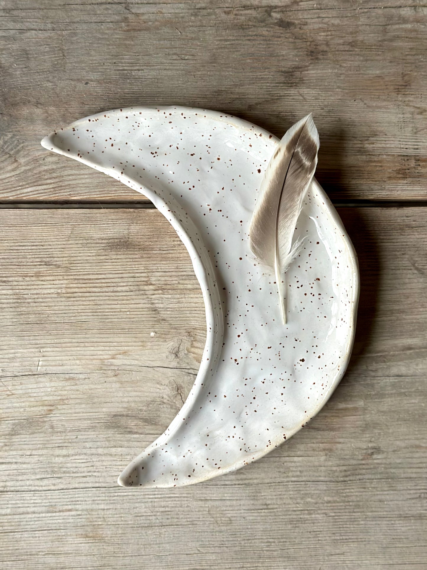 Moon shaped decorative tray in white color. On the tray lays a feather.