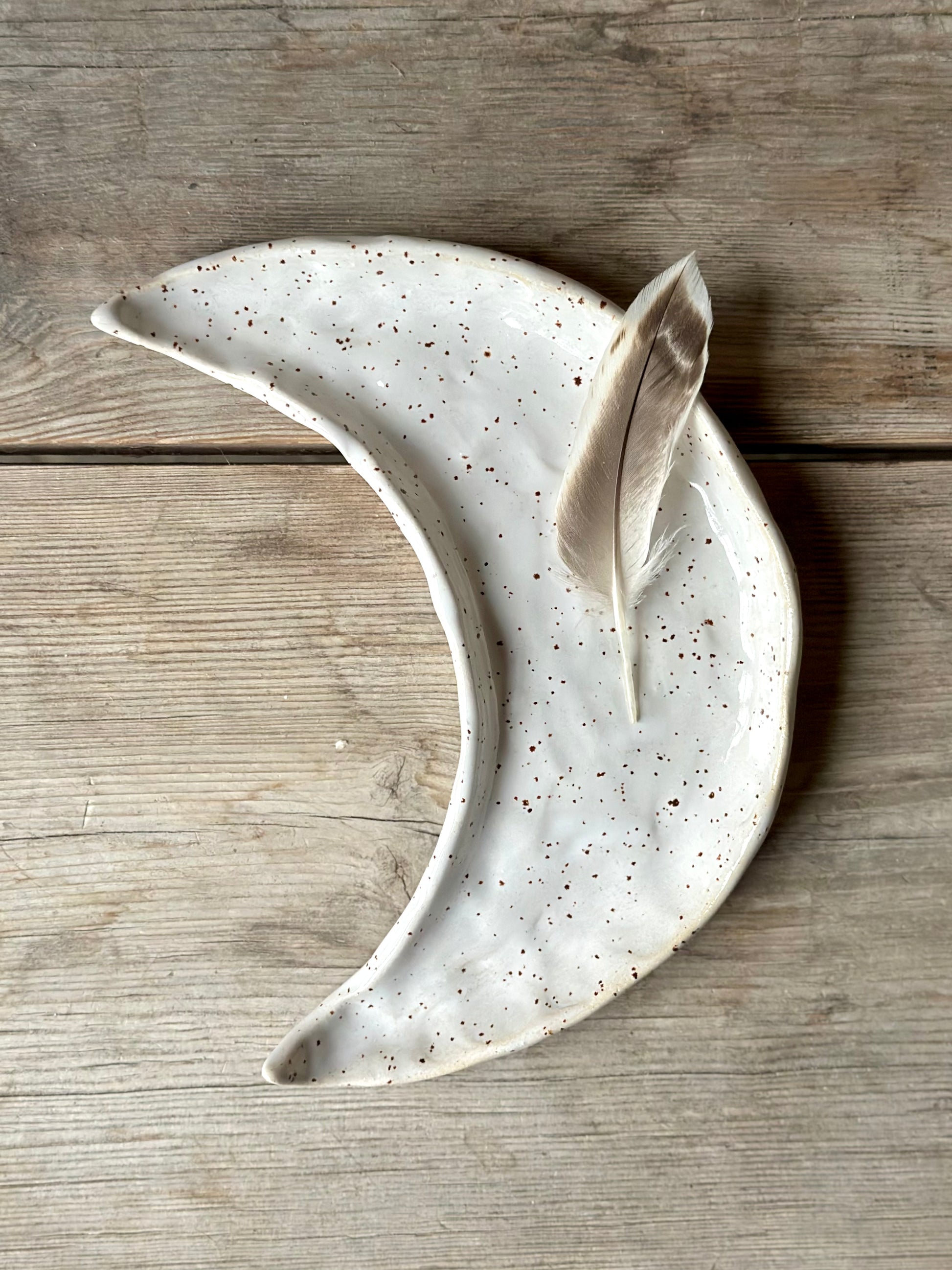 Moon shaped decorative tray in white color. On the tray lays a feather.