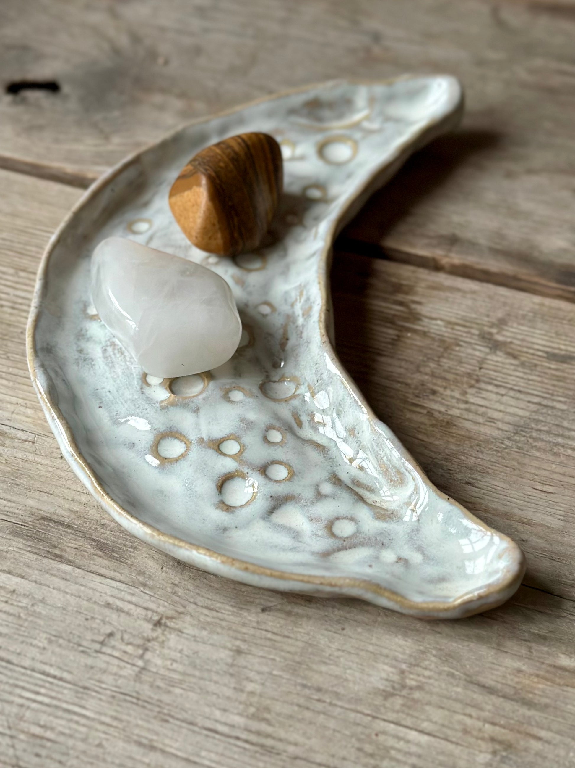 Moon shaped decorative tray in light beige and white color. On the tray lays chrystal stones.