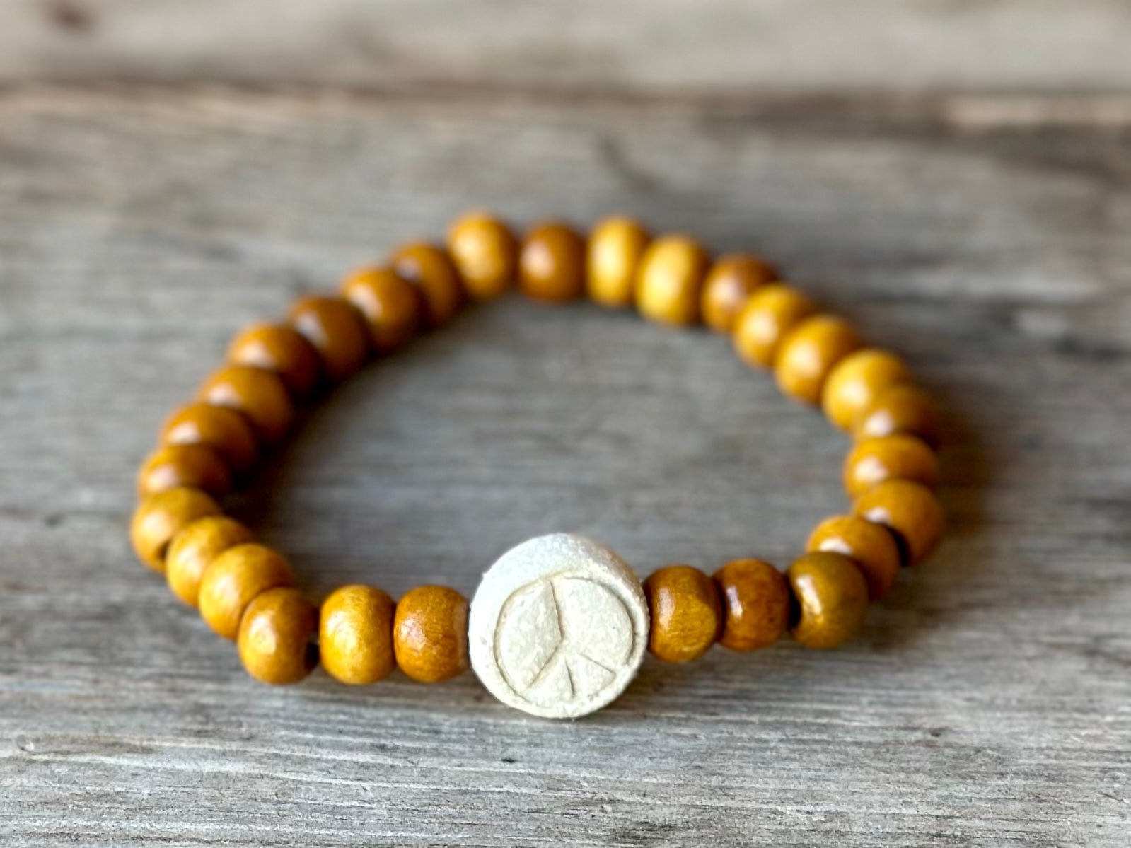 Studio Meraki bacelet with wood pearls and a raw ceramic pearl with a peace sign. 