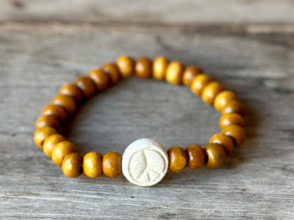 Studio Meraki bacelet with wood pearls and a raw ceramic pearl with a peace sign. 