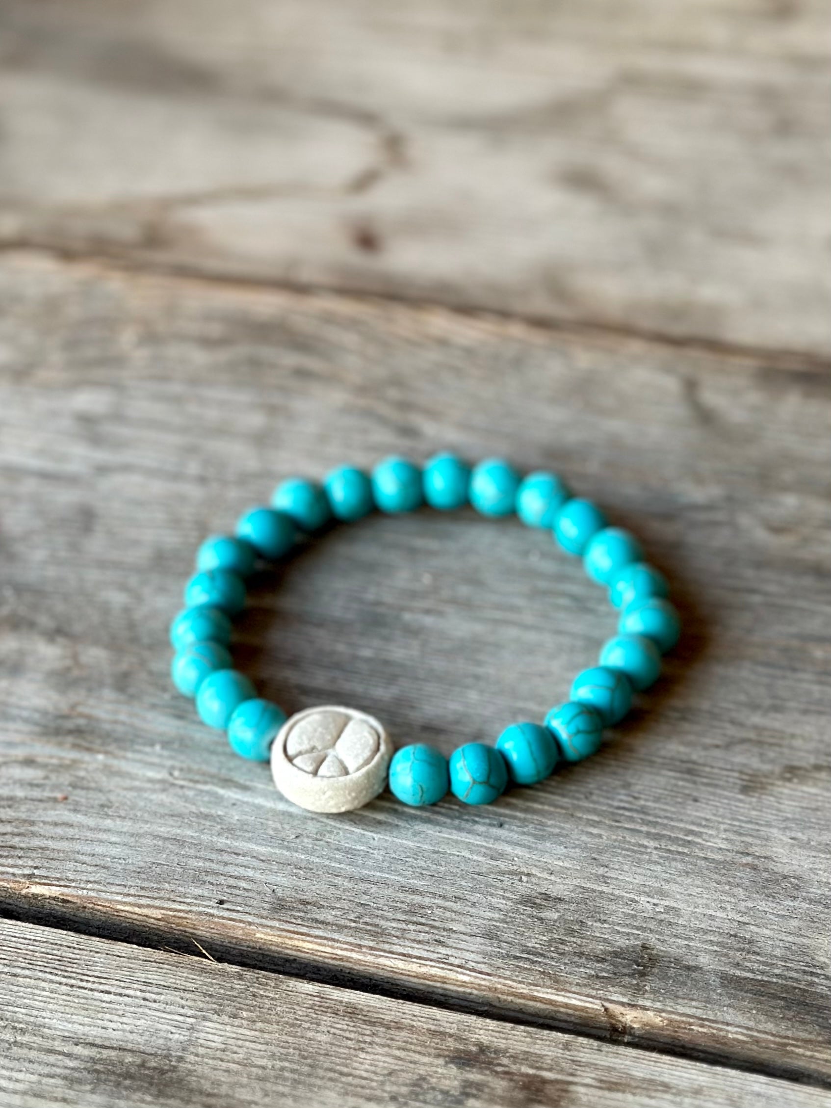 Studio Meraki bacelet with turqoise chrystal pearls and a raw ceramic pearl with a peace sign. 