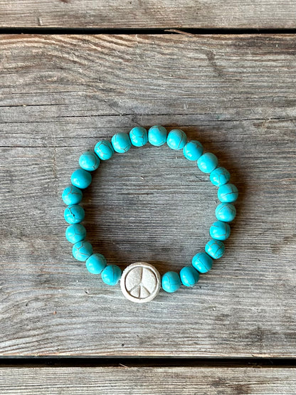 Studio Meraki bacelet with turqoise chrystal pearls and a raw ceramic pearl with a peace sign. 