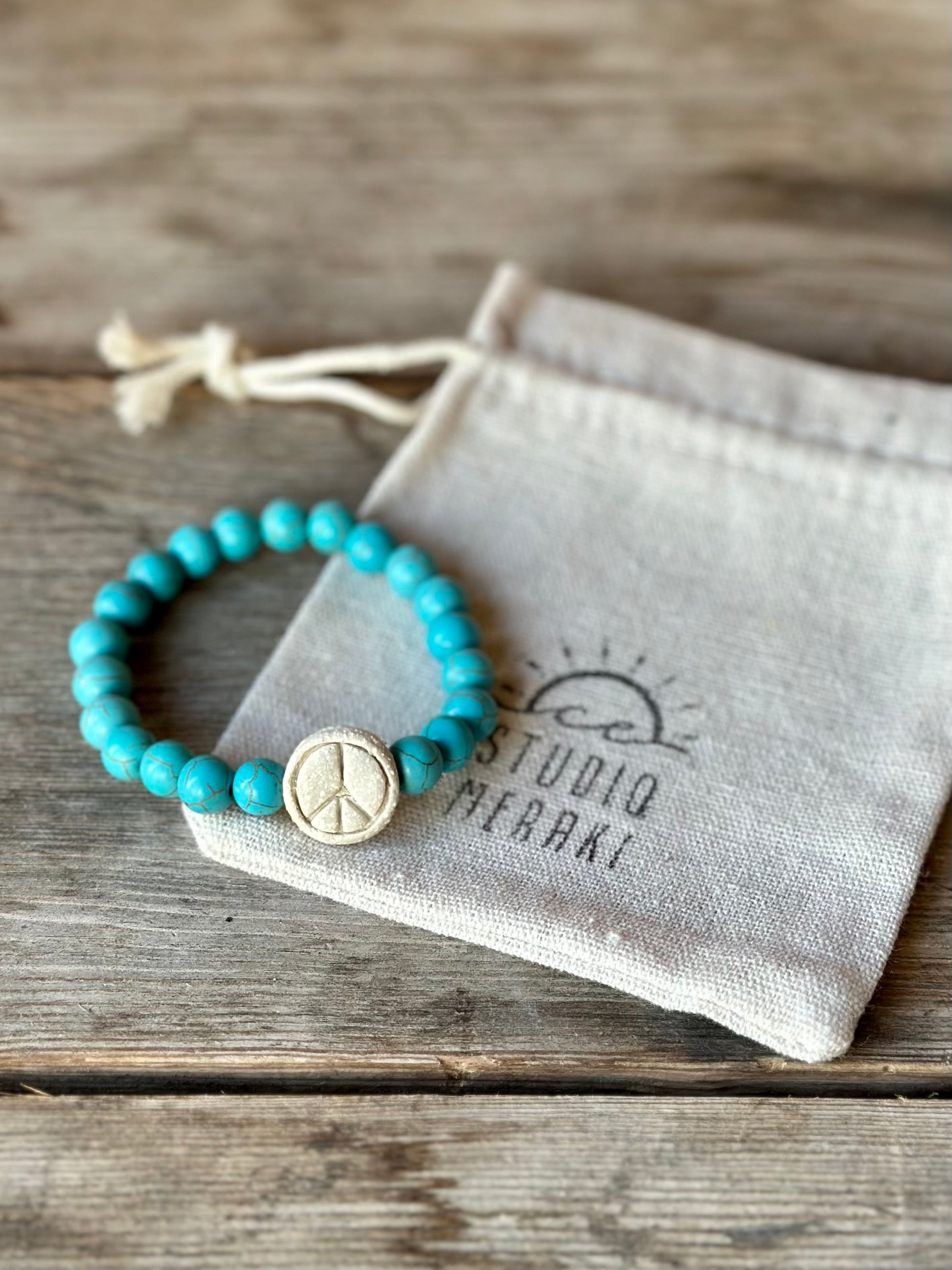 Studio Meraki bacelet with turqoise chrystal pearls and a raw ceramic pearl with a peace sign. 