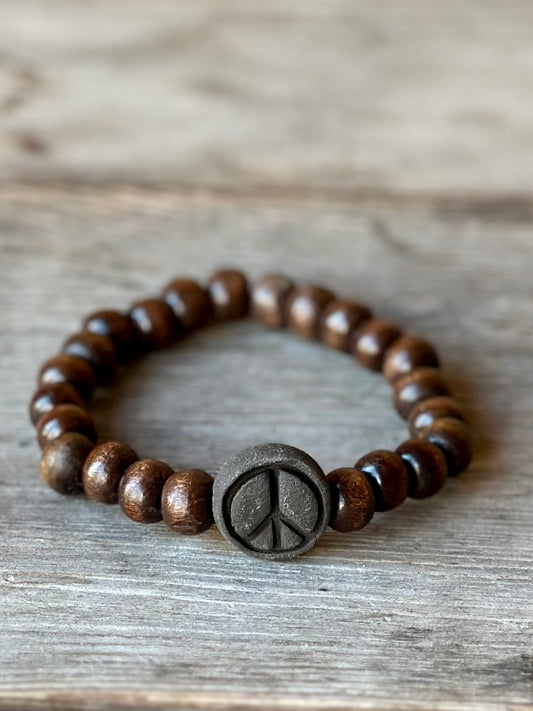 Studio Meraki bacelet with wood pearls and a raw ceramic pearl with a peace sign. 