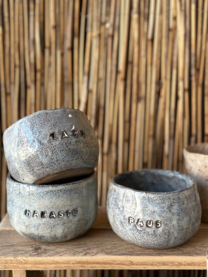 Ceramic mugs on a shelf. Decorated with words like Pause and Namaste.