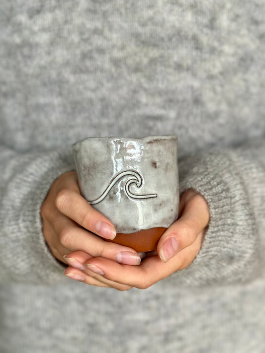 Female hands holding a ceramic mug decorated with a wave