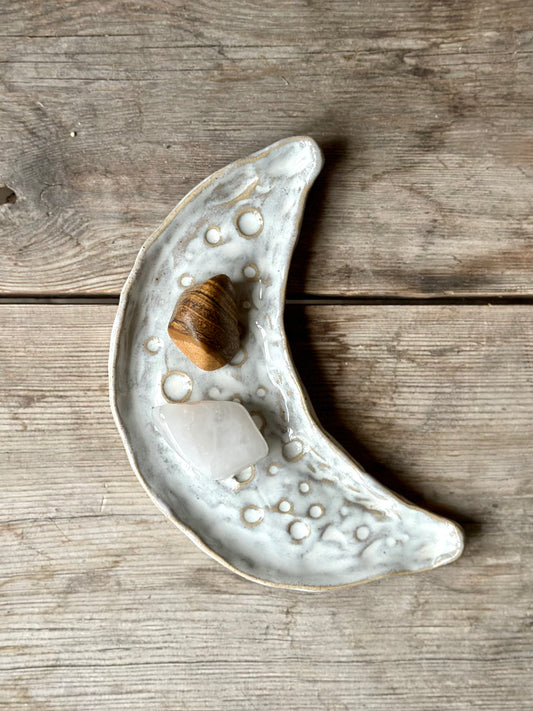 Moon shaped decorative tray in light beige and white color. On the tray lays chrystal stones.