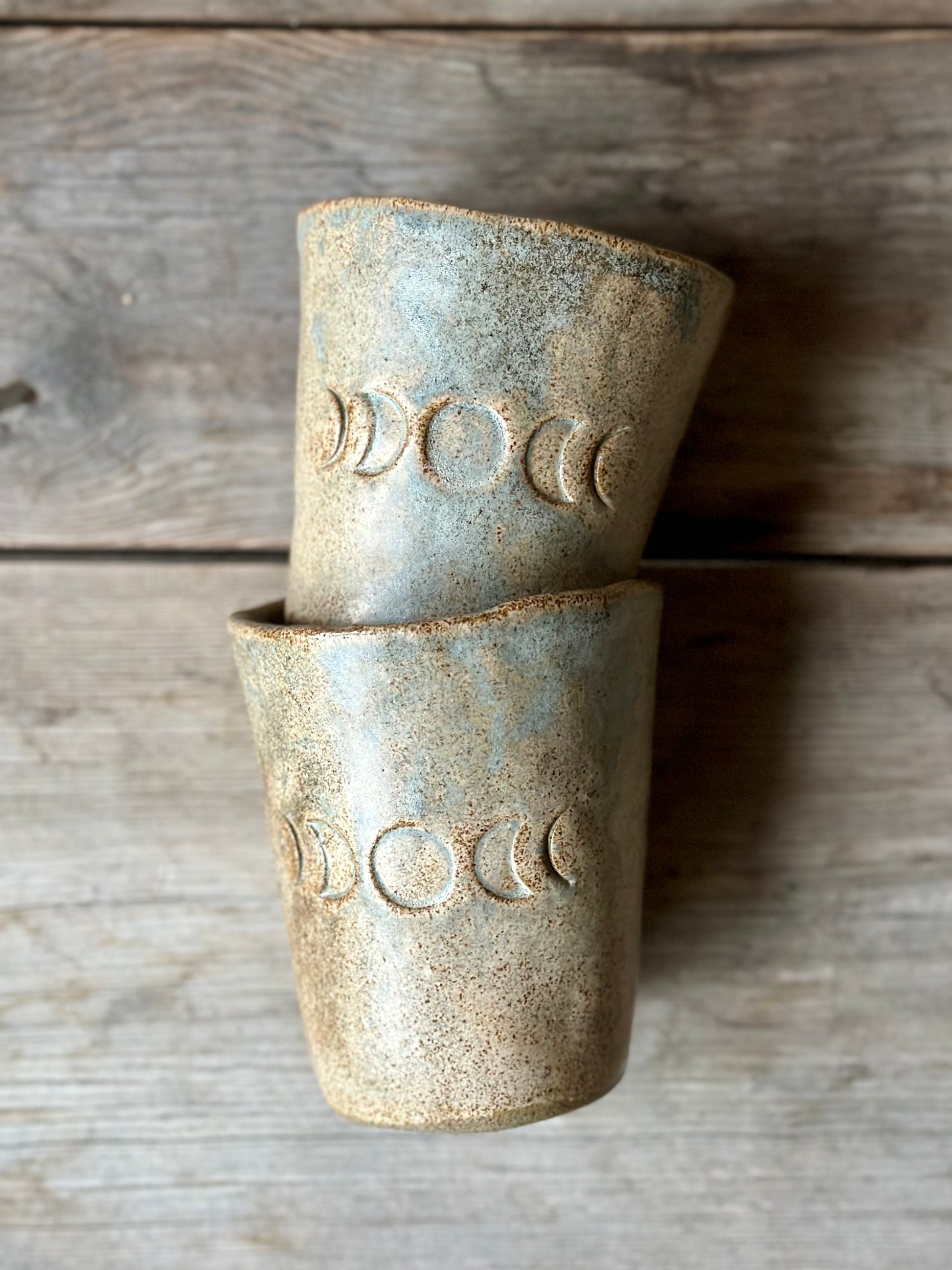 Beige grey ceramic cups laying on a grey old table. The cups is decorated with moon phases.