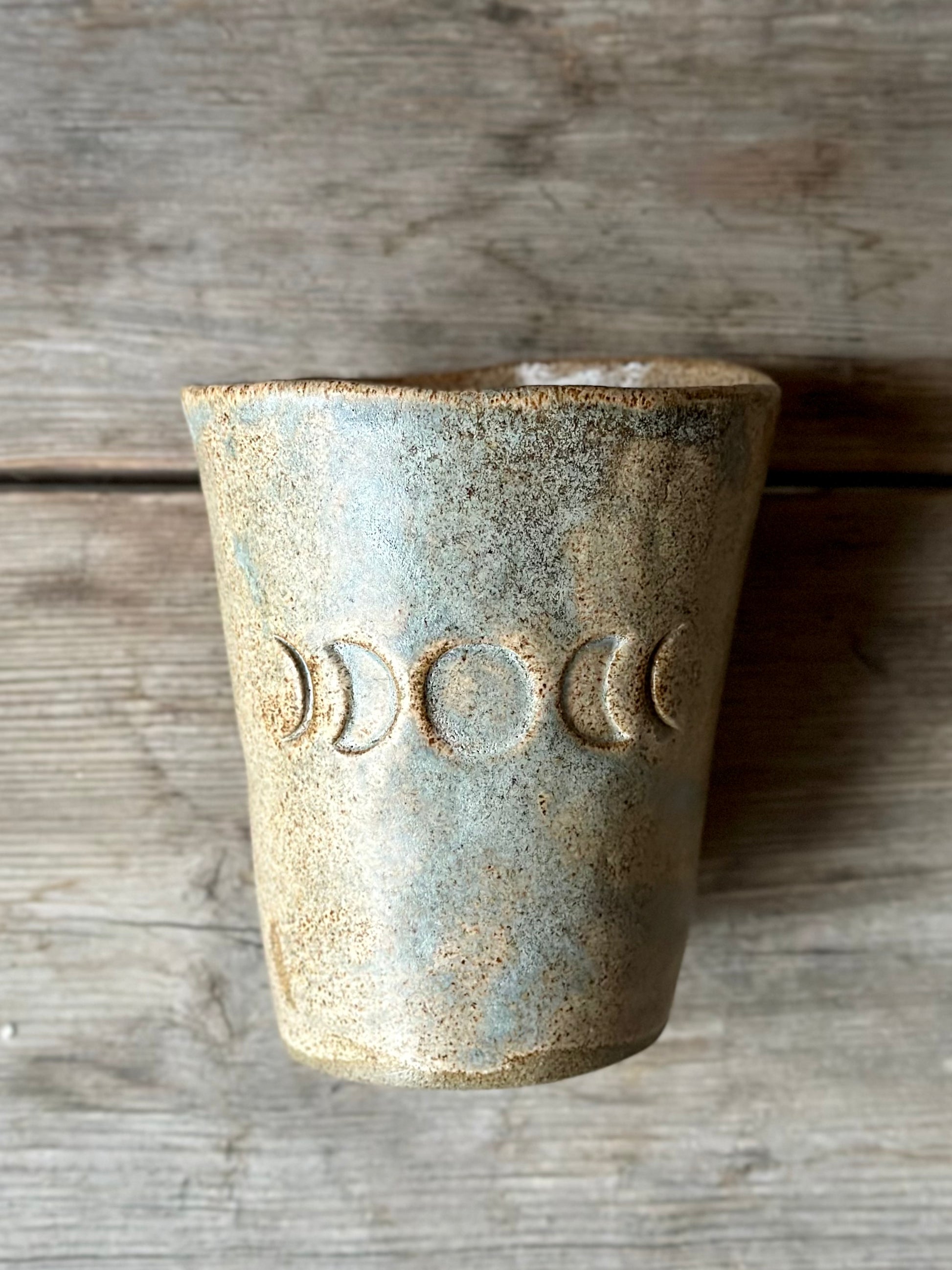Beige grey ceramic cup laying on a grey old table. The cup is decorated with moon phases. 