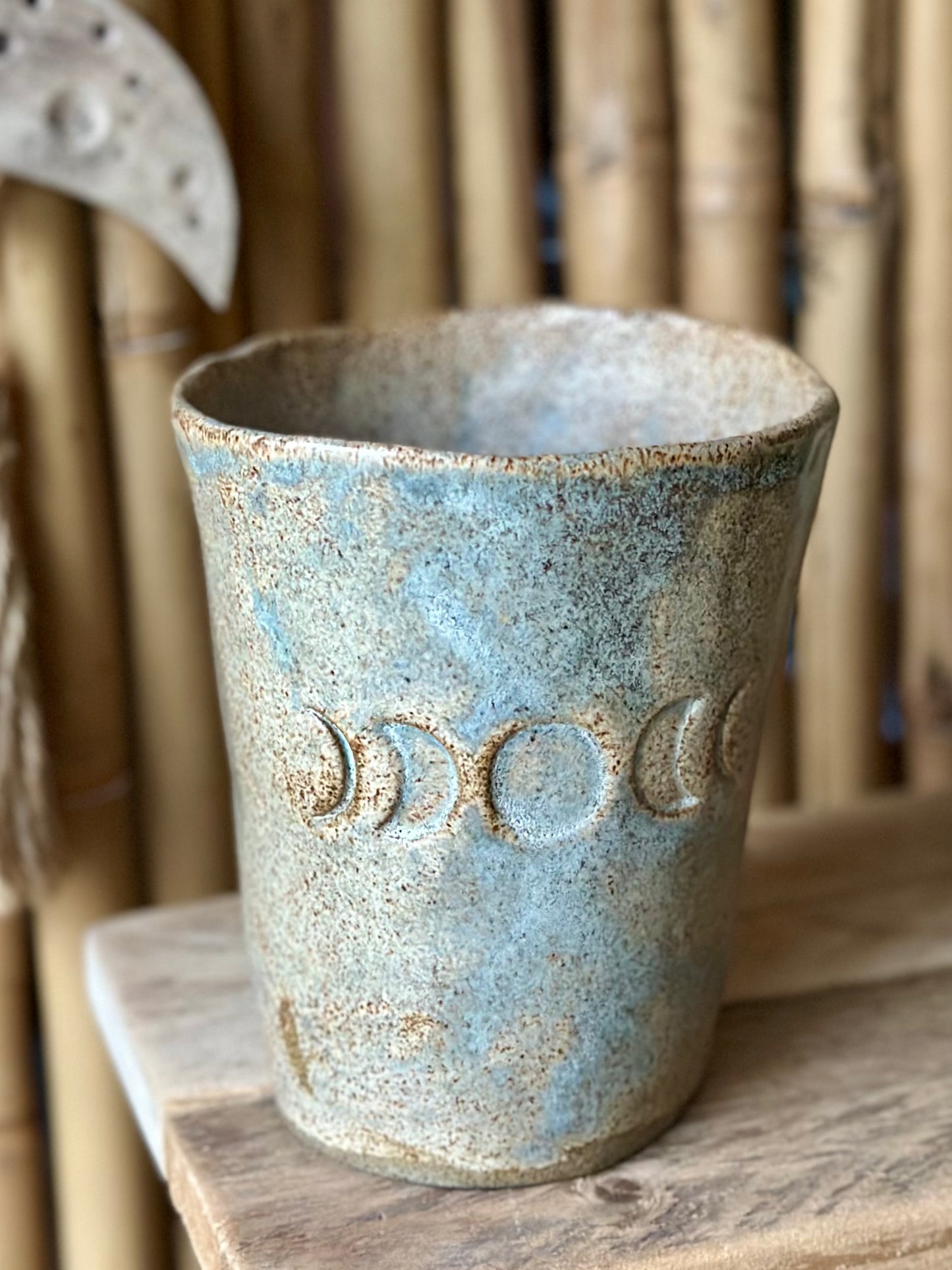 Beige grey ceramic cup decorated with the moon phases, standing on a shelf.