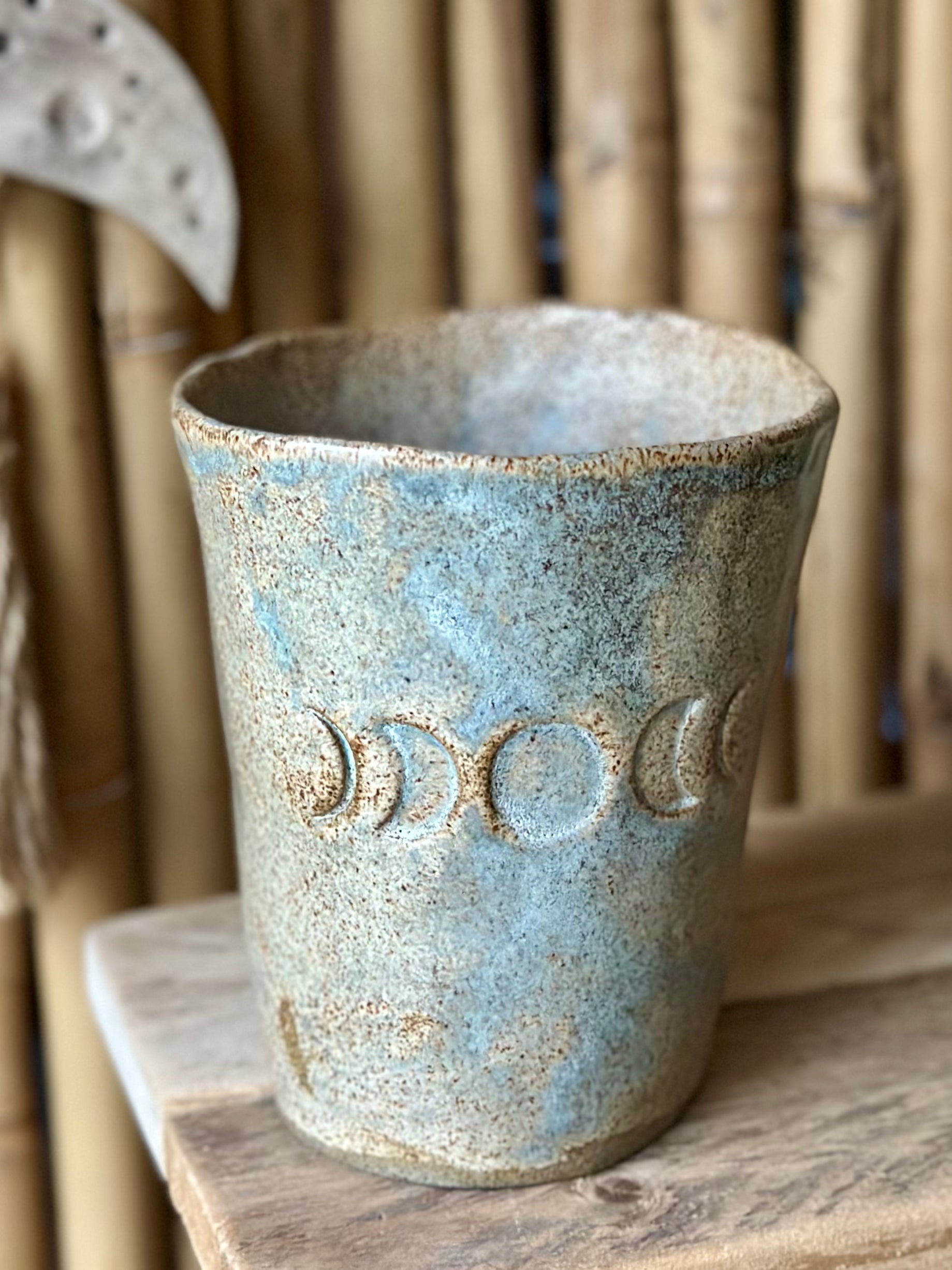 Beige grey ceramic cup decorated with the moon phases, standing on a shelf.